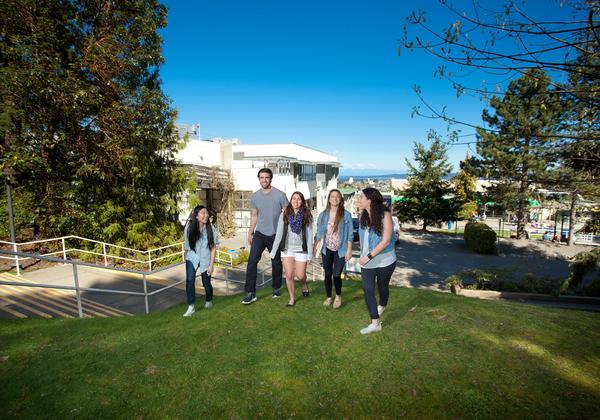 group of five young people walking up a grassy hill with blue sky in background