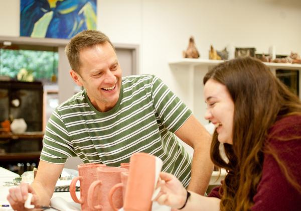 male instructor sits with female student at table covered with ceramics
