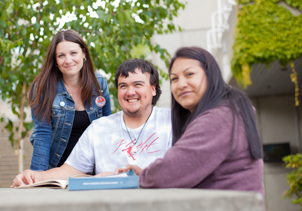two young woman sit with a young man at a table outdoors